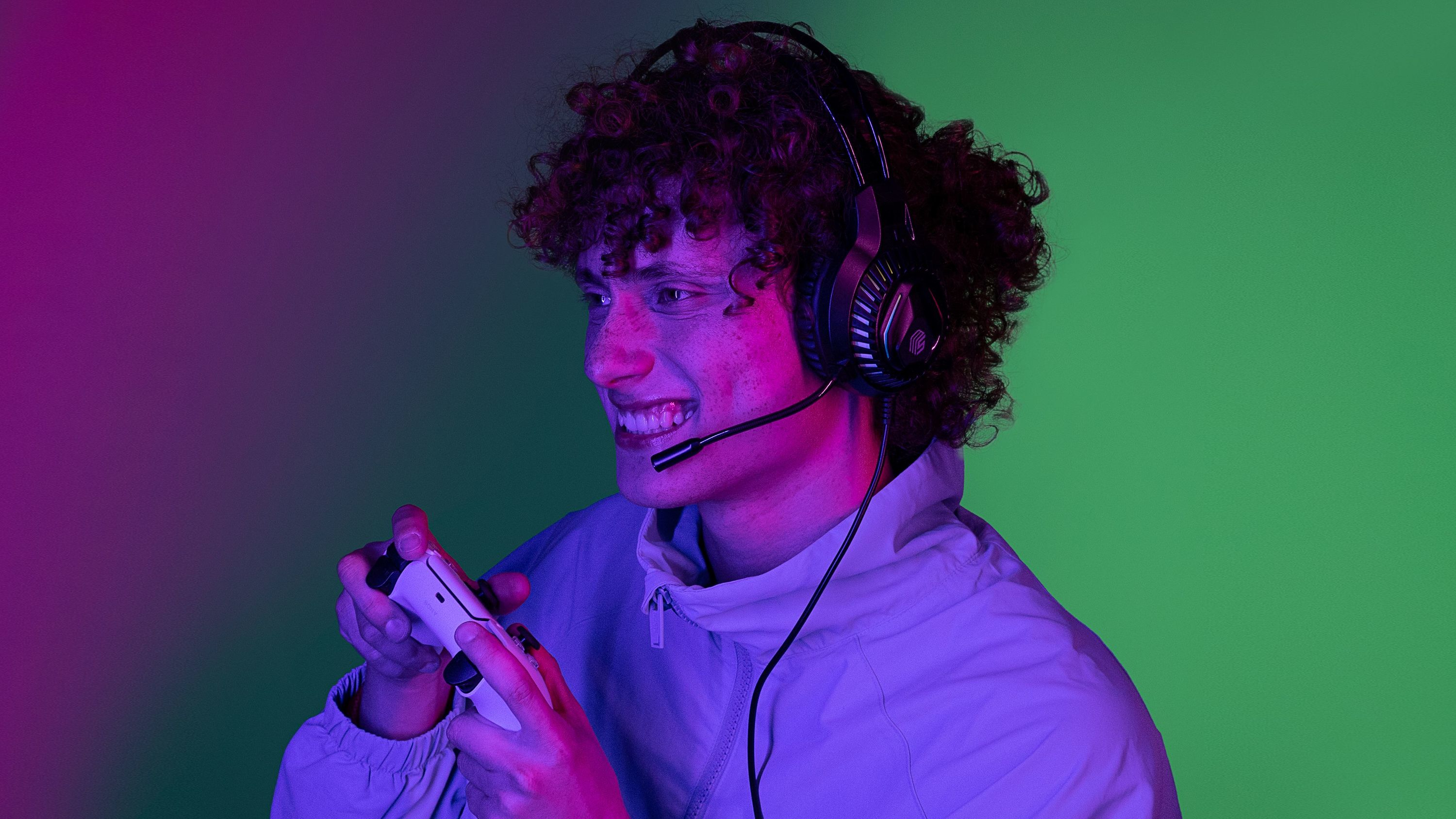 Junger Mann mit Headset spielt mit Controller unter lila und grünem Licht.