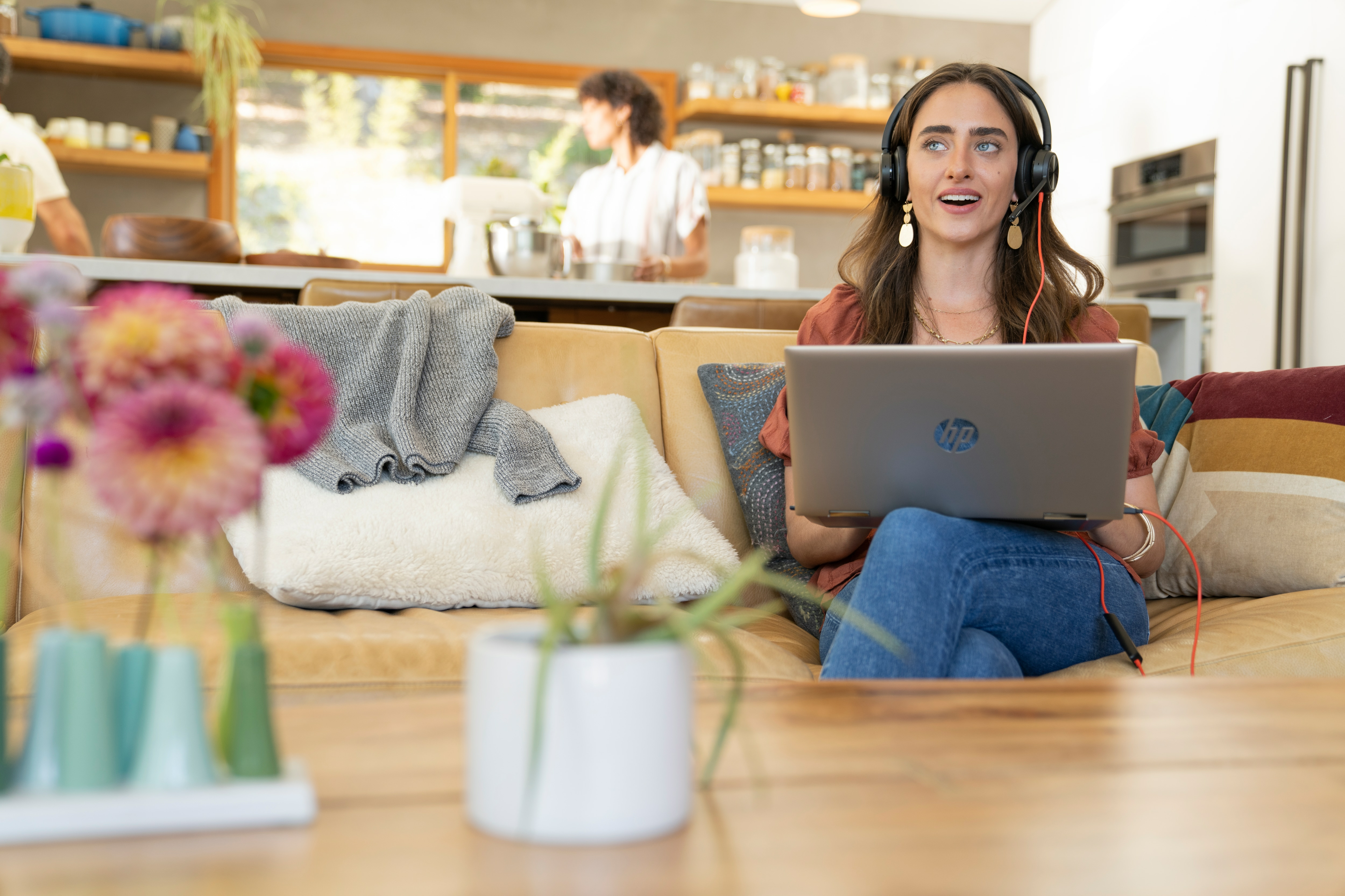 Una donna usa un laptop con un auricolare. È seduta su un divano in un salotto.