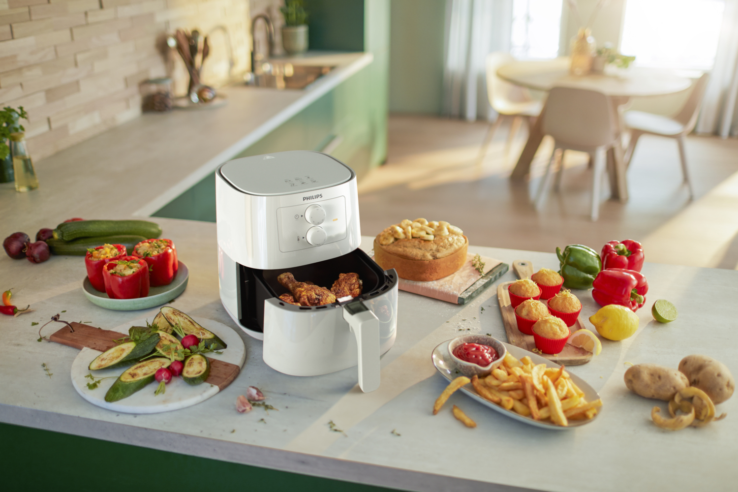 Friggitrice ad aria con cibo, tra cui pollo e patatine fritte. Vari ingredienti sul piano cucina.