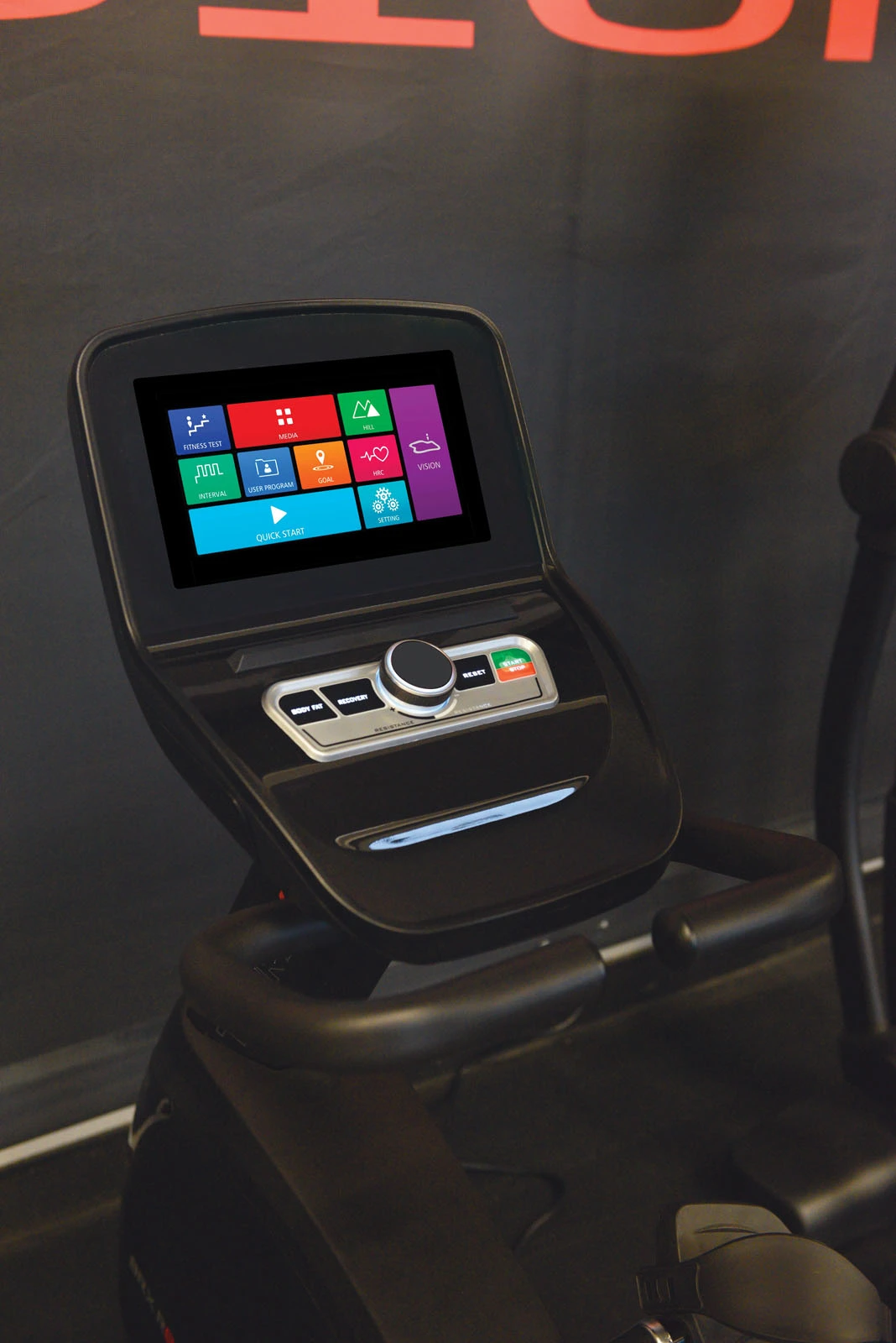 Gros plan sur la console d'un vélo d'exercice noir avec un écran affichant plusieurs options d'entraînement.