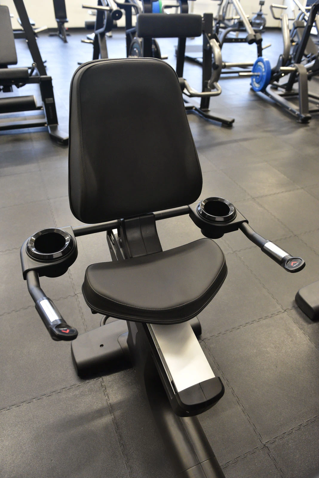 Vélo d'exercice couché avec siège et poignées noirs dans un cadre de gym.