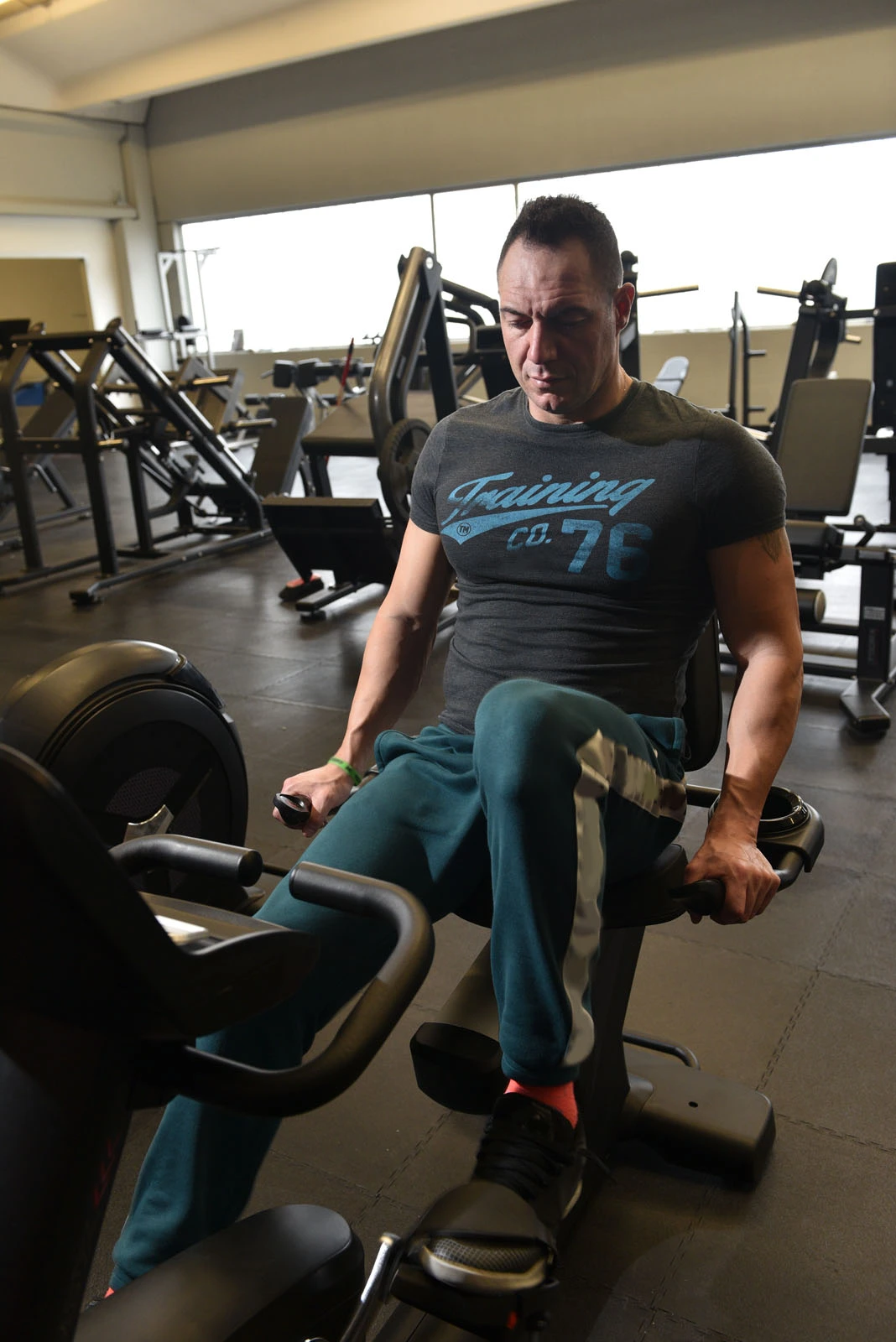 Un homme dans une salle de sport, sur un vélo d'exercice, en t-shirt et short.