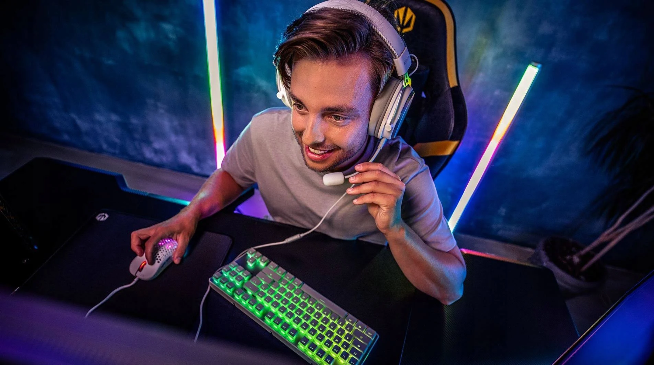 Mężczyzna w zestawie słuchawkowym do gier, uśmiechnięty podczas grania na komputerze z klawiaturą i myszą.