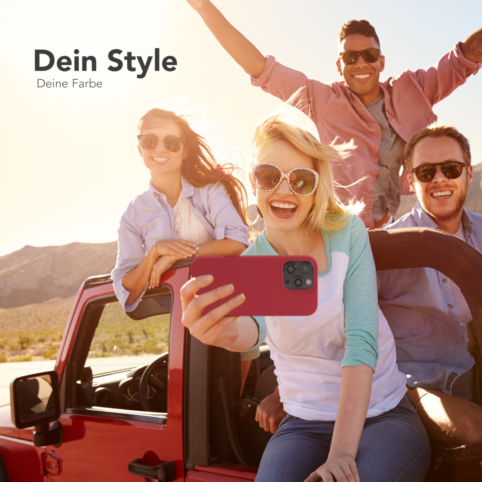 Eine Gruppe Freunde in einem roten Jeep machen ein Selfie. Der Hintergrund zeigt eine Wüstenlandschaft bei Sonnenlicht.