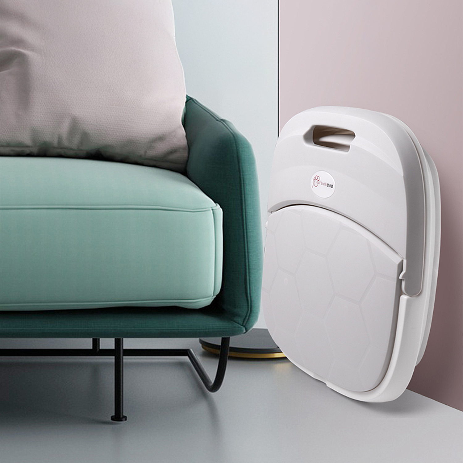 Orinal plegable blanco apoyado en pared rosa junto a sofá verde.