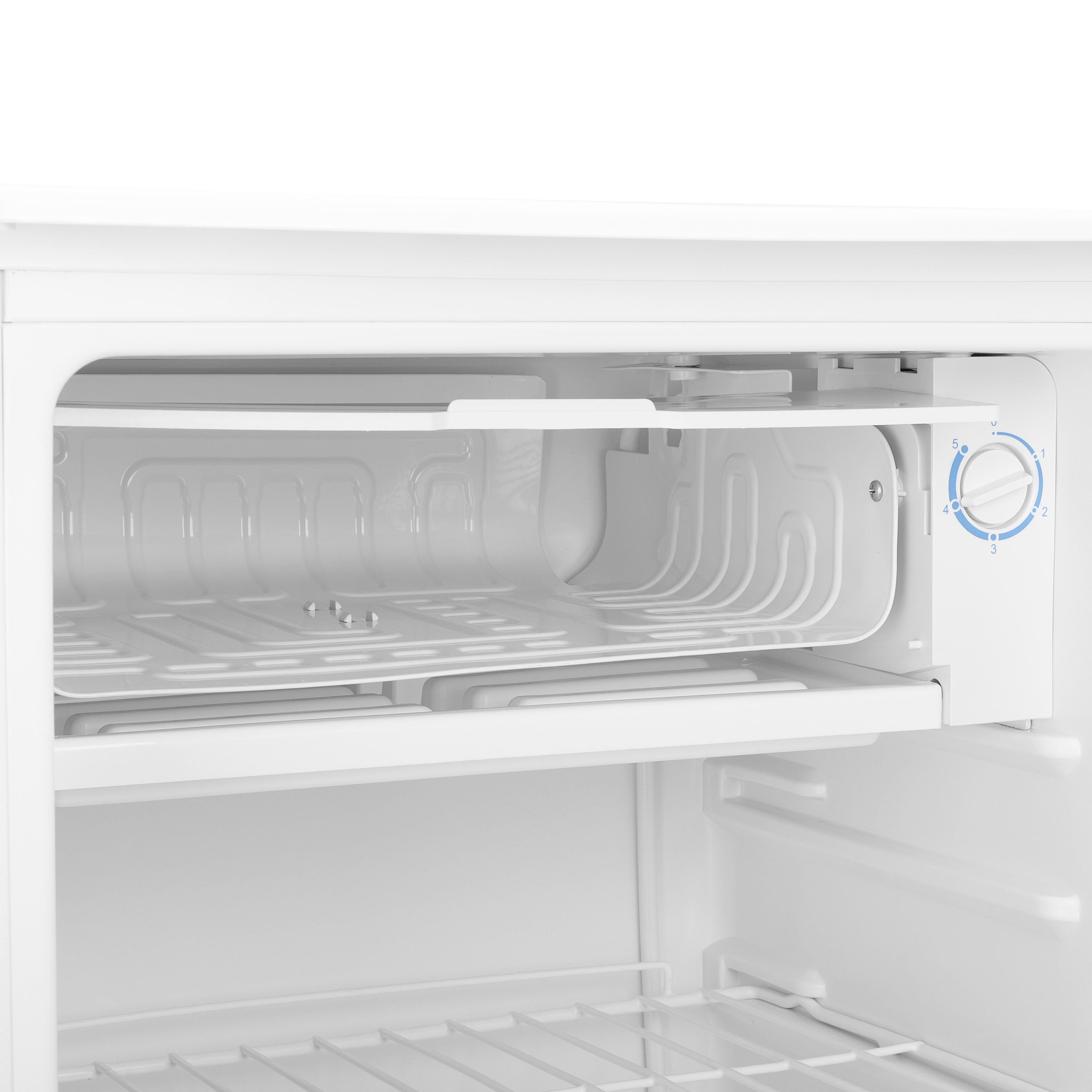 Interior de una mini-nevera blanca. Muestra estantes y un dial de control de temperatura a la derecha.