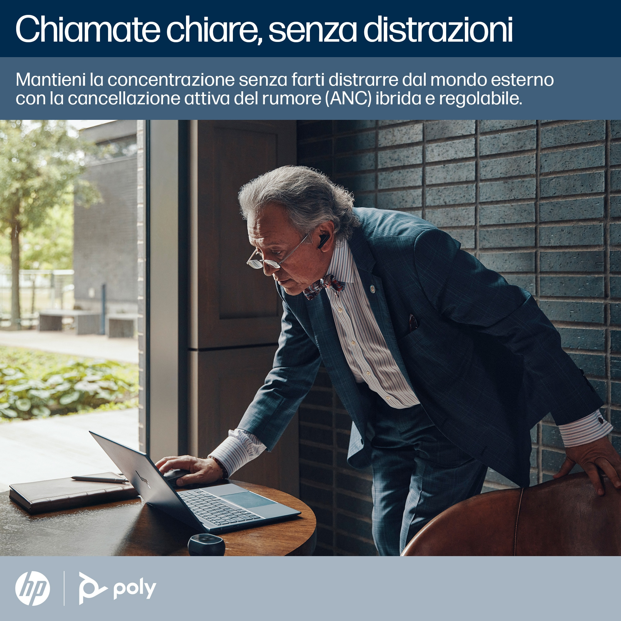 Un uomo in giacca e cravatta con gli occhiali guarda un laptop. La scena è in interni.