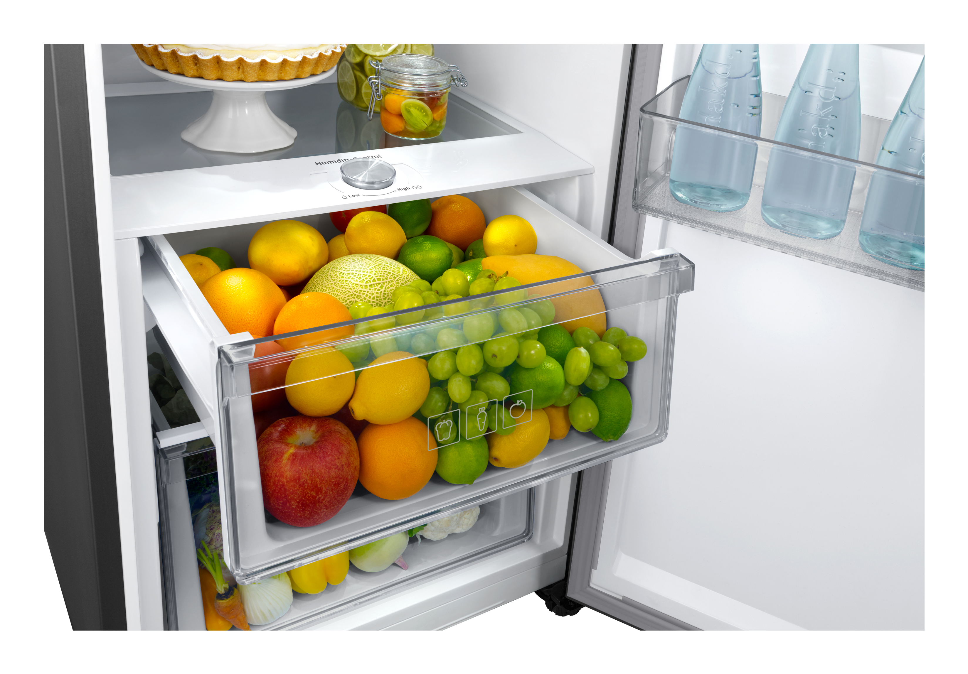 Interno del frigorifero con cassetto frutta, contenente vari frutti. Ripiani trasparenti con bottiglie.