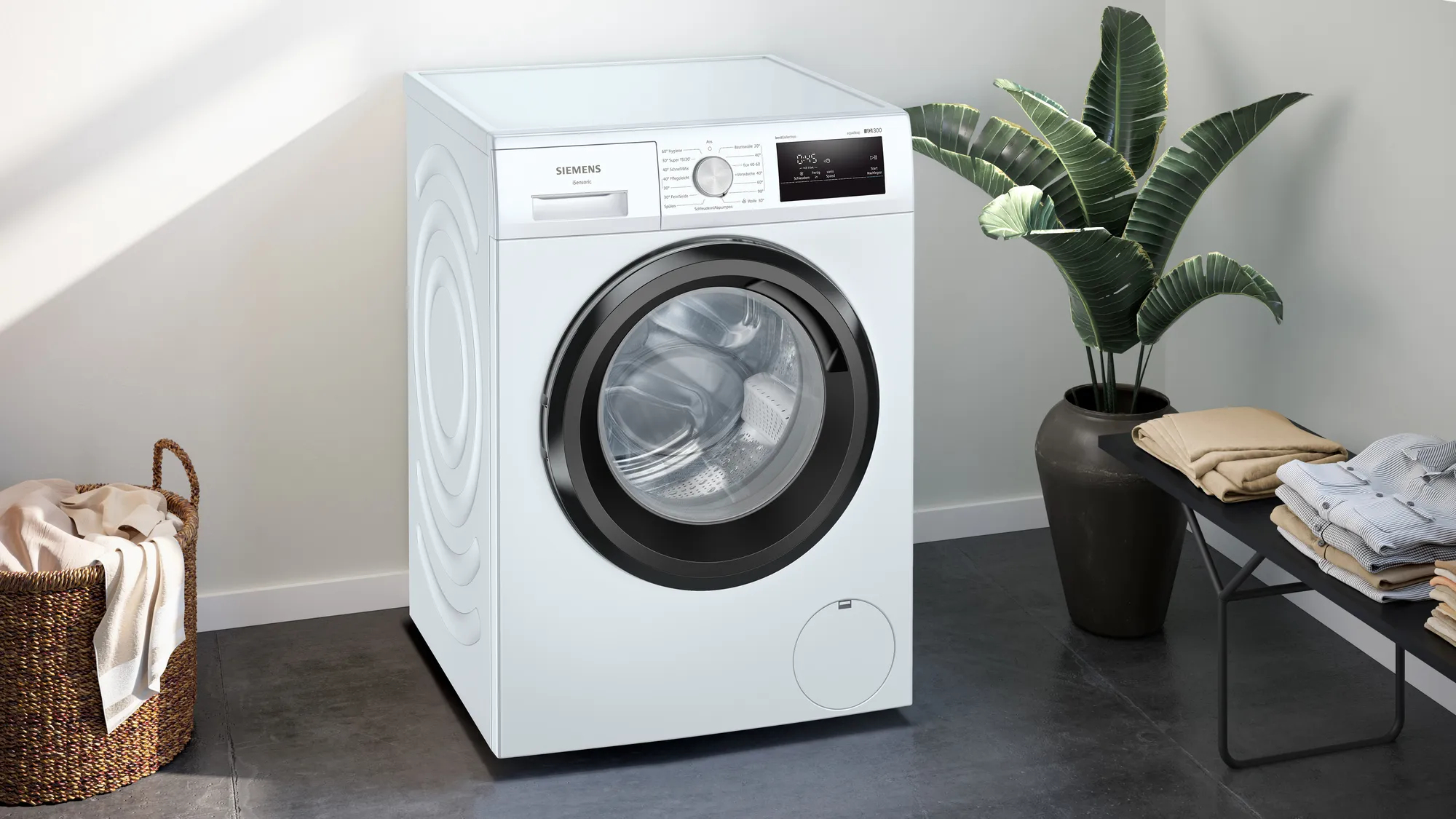 Eine weiße Siemens Waschmaschine neben einer Pflanze und einem Korb mit Kleidung.