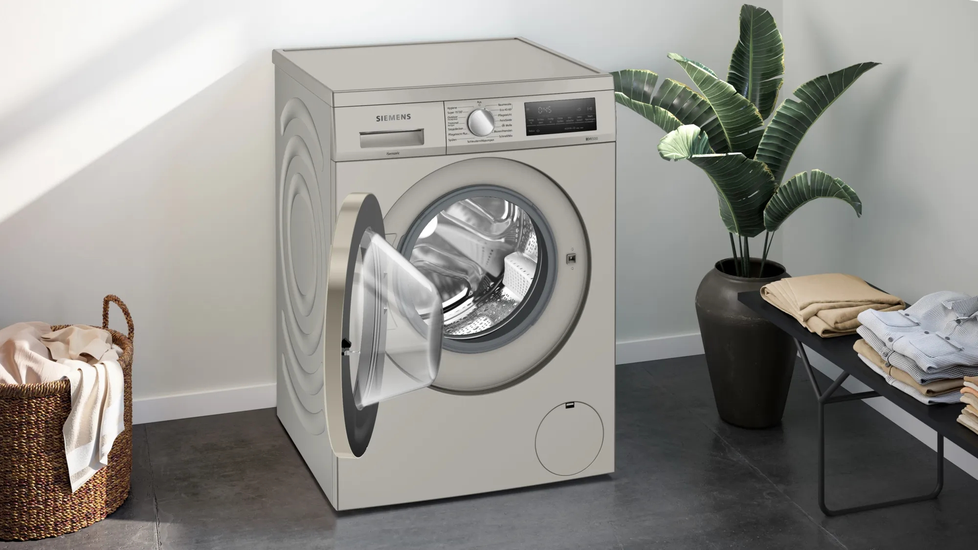 Waschmaschine mit offener Tür. Wäschekorb und Pflanzen im Hintergrund.