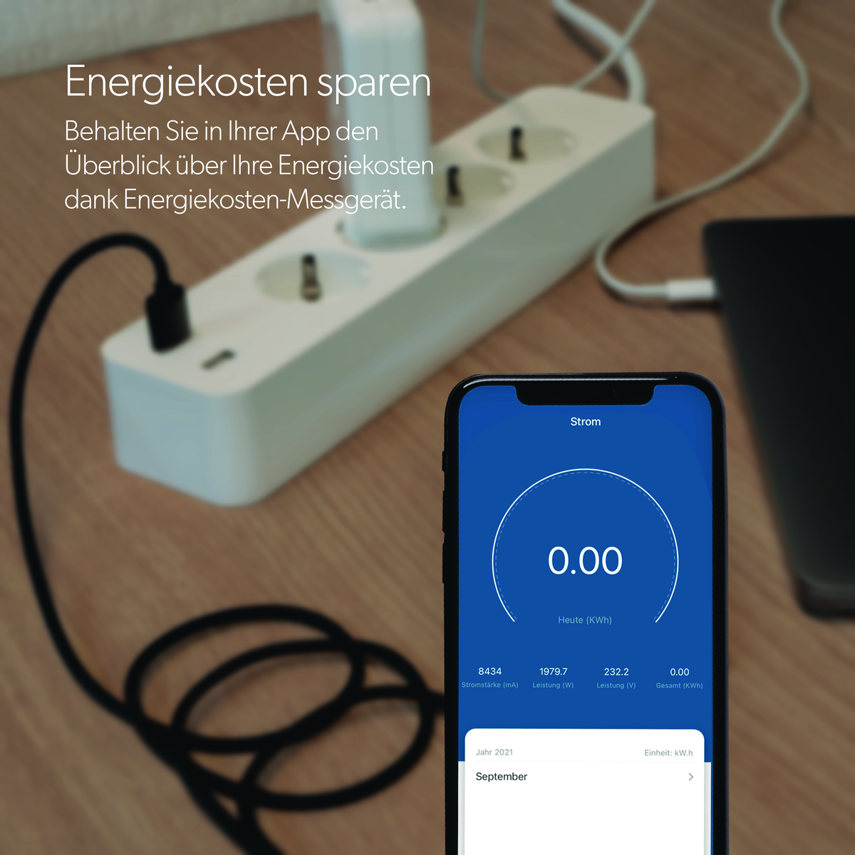 Ein Telefon, das den Energieverbrauch anzeigt, eine Steckdosenleiste und ein Laptop auf einem Tisch.