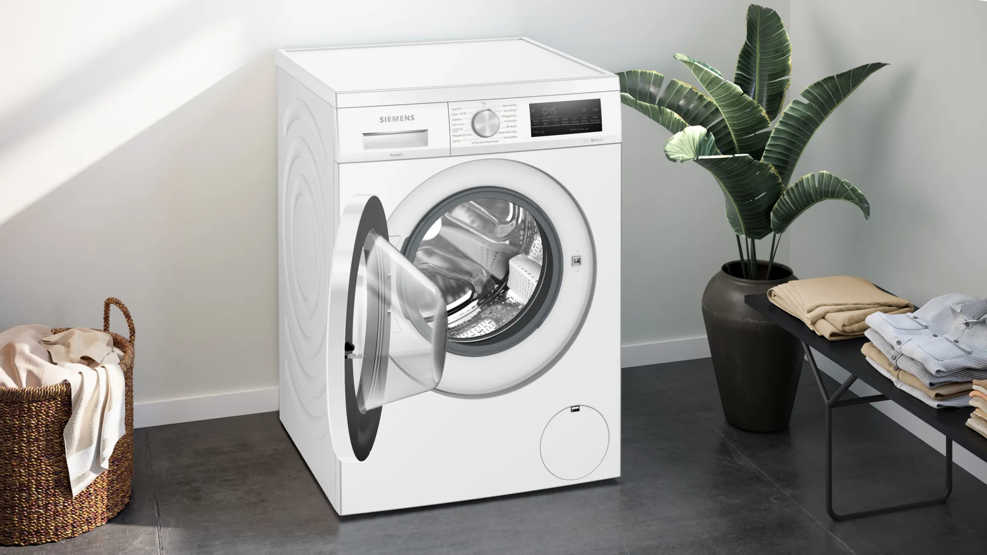 Weiße Siemens Waschmaschine mit offener Tür, neben einer Pflanze und Kleidung auf einem Gestell.