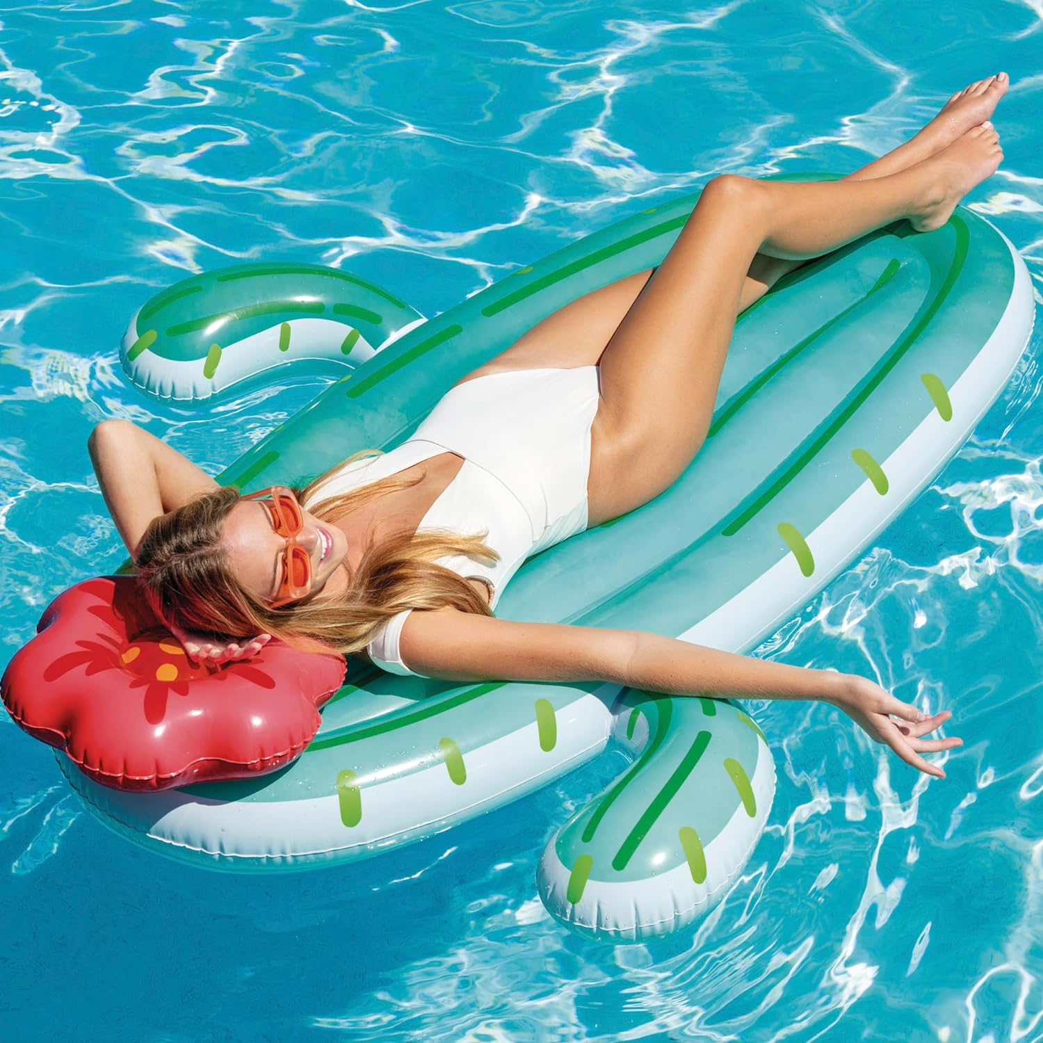 Una donna in costume da bagno bianco sdraiata su un galleggiante a forma di cactus in una piscina.