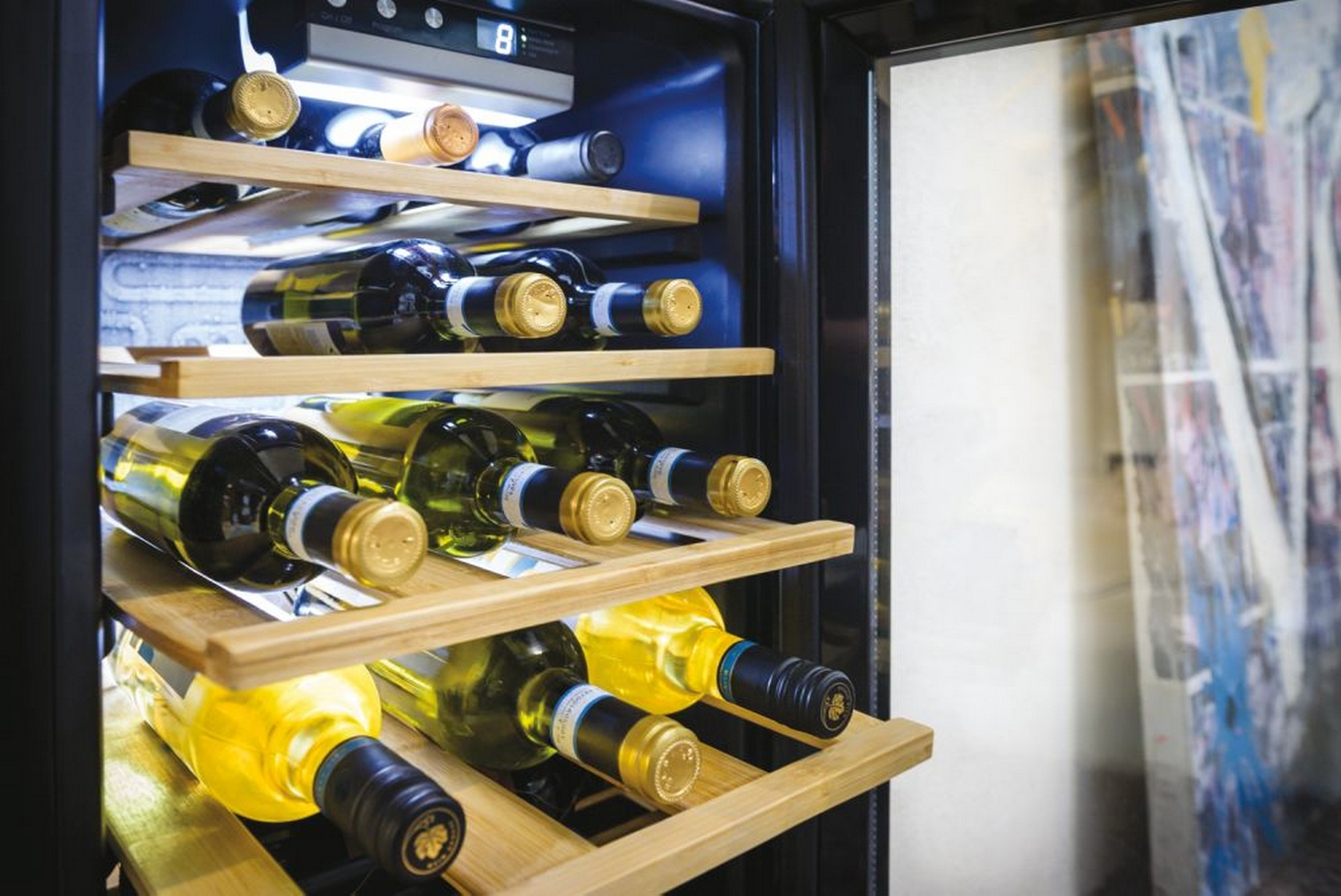 Una cantinetta Candy, con una porta a vetri che mostra bottiglie su ripiani in legno, una maniglia laterale.
