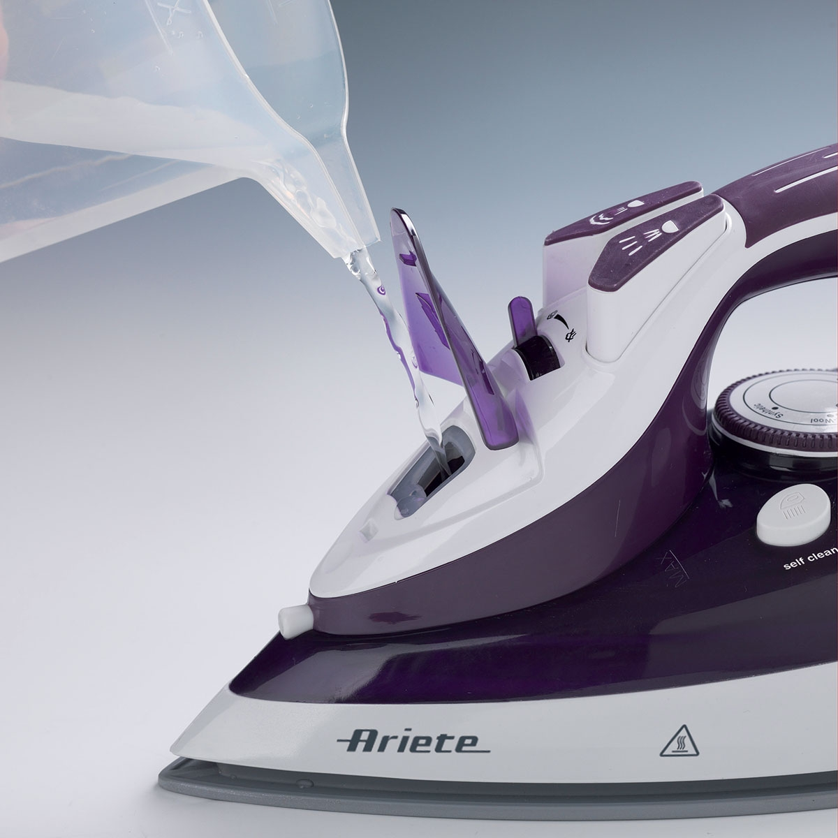 Un ferro da stiro viola e bianco viene riempito d'acqua da una brocca.