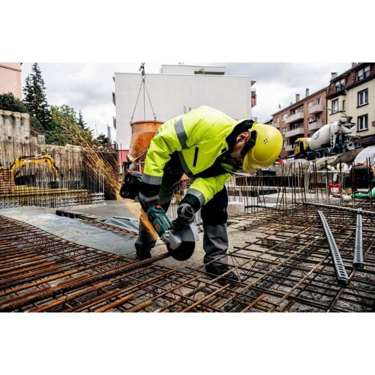Un ouvrier du bâtiment meulant des barres d'armature sur un chantier, des étincelles volent. Il porte des équipements de sécurité.