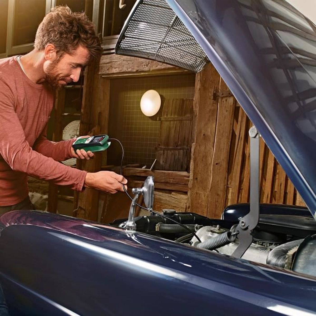 Ein Mann arbeitet an einem Automotor. Er hält ein Gerät, und die Motorhaube ist offen.