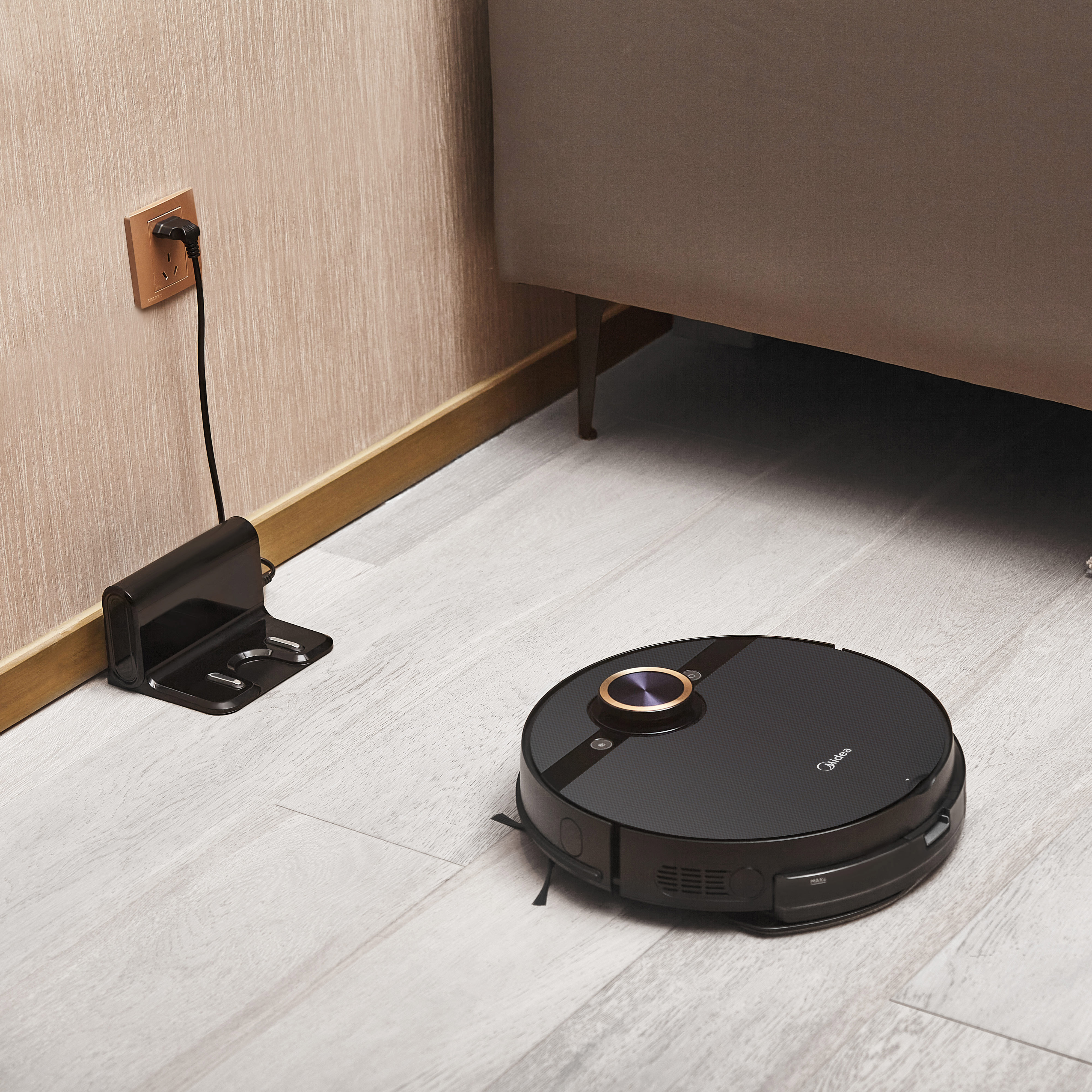 Czarny robot odkurzający na drewnianej podłodze obok stacji ładującej.