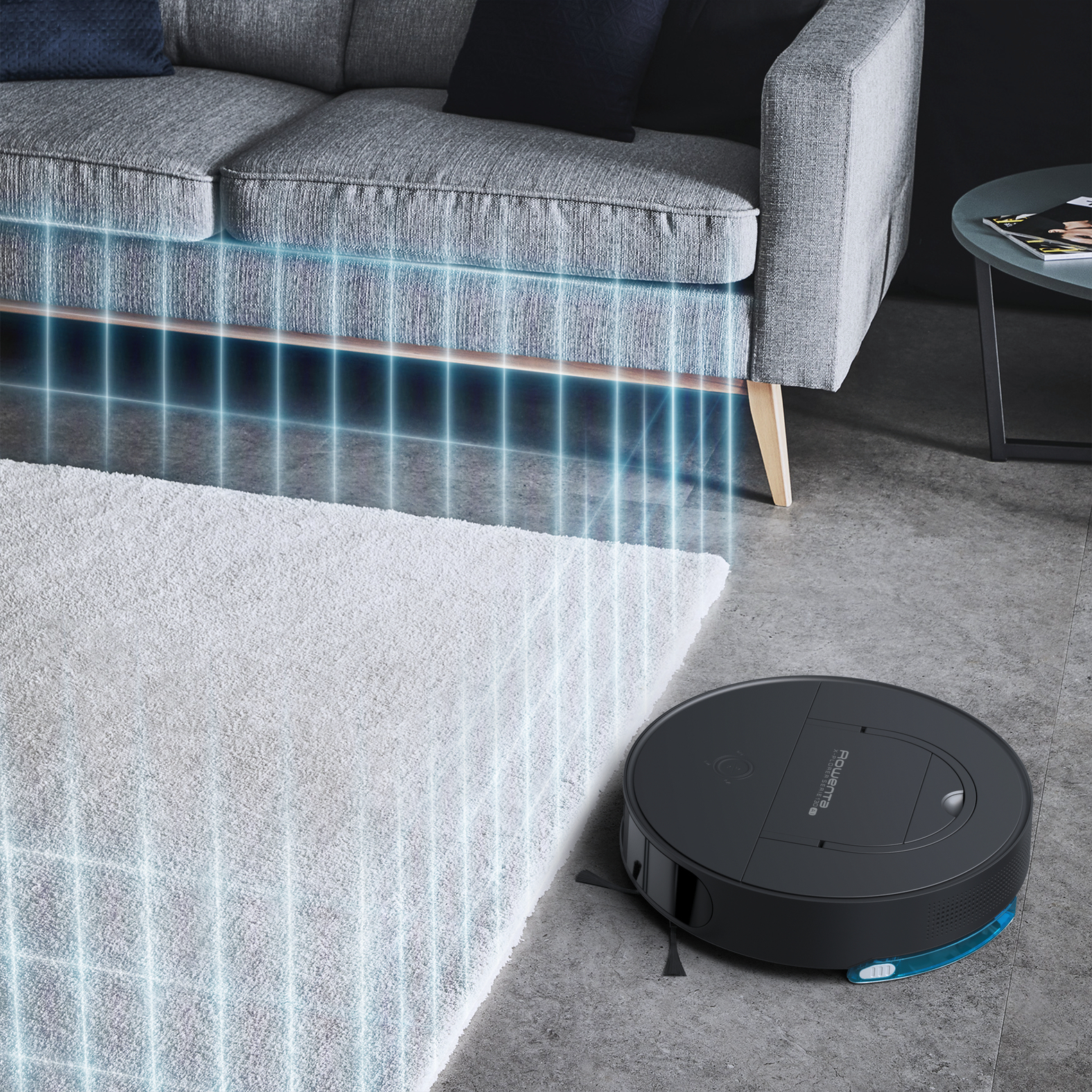 Robot sprzątający na podłodze. Szara sofa i biały dywan. Niebieskie światło od odkurzacza.