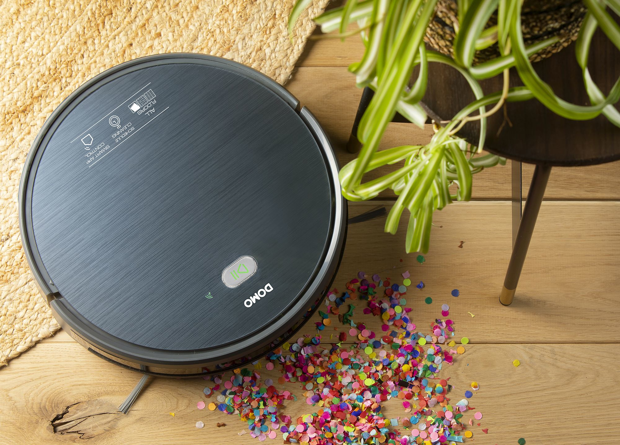 Un aspirateur robot gris foncé avec des confettis sur le sol.