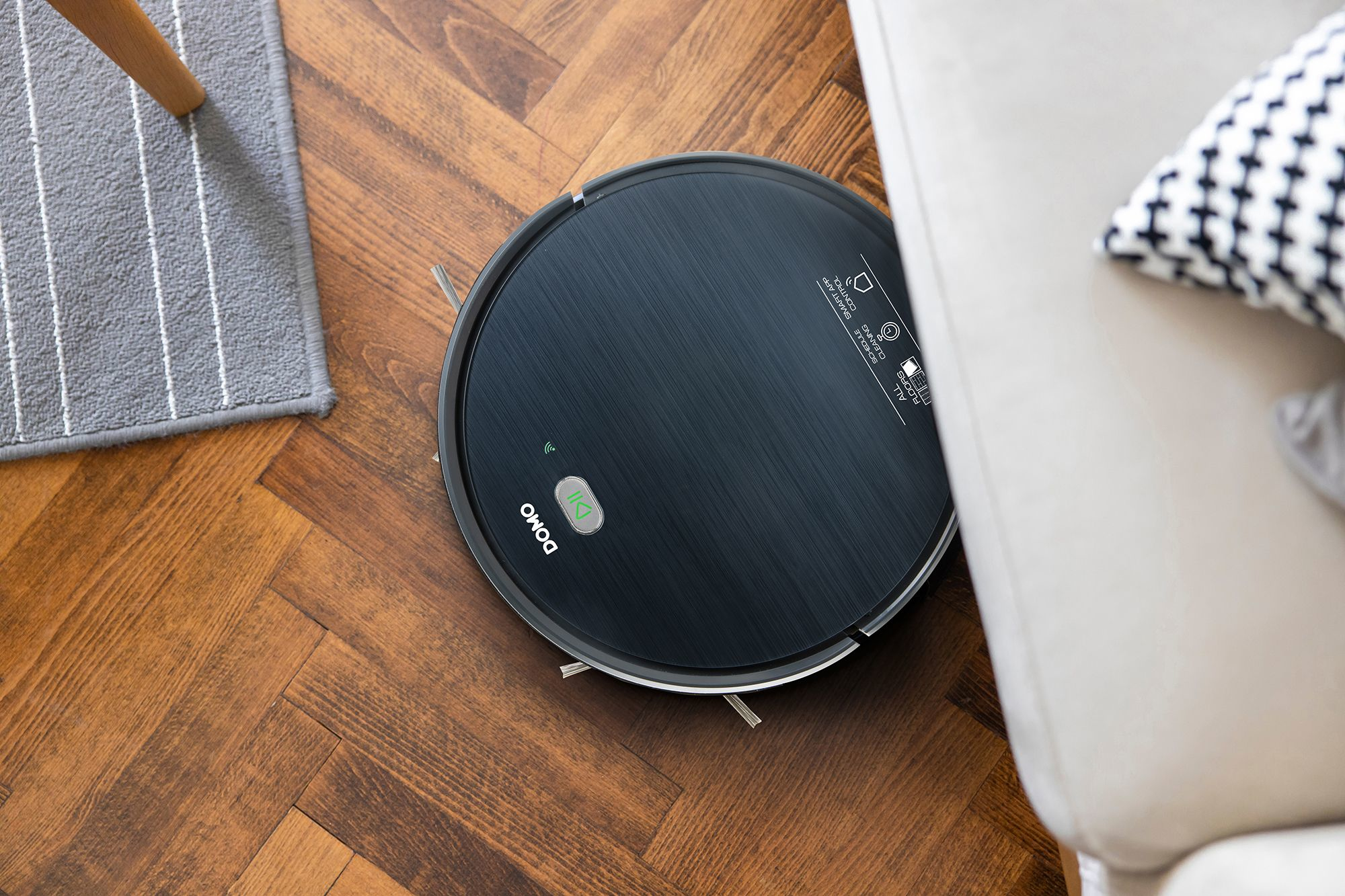 Un aspirateur robot noir sur un sol en bois à côté d'un canapé.