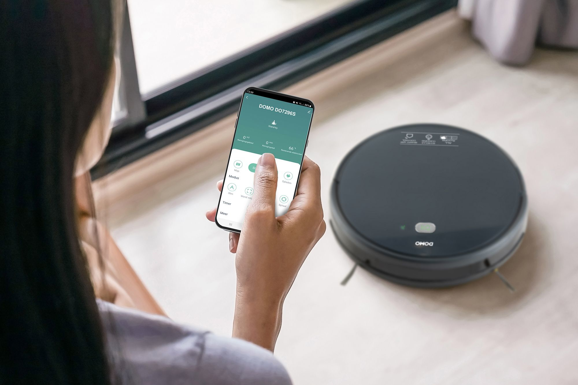 Femme utilisant un téléphone pour contrôler un aspirateur robot DOMO noir sur un plancher en bois.