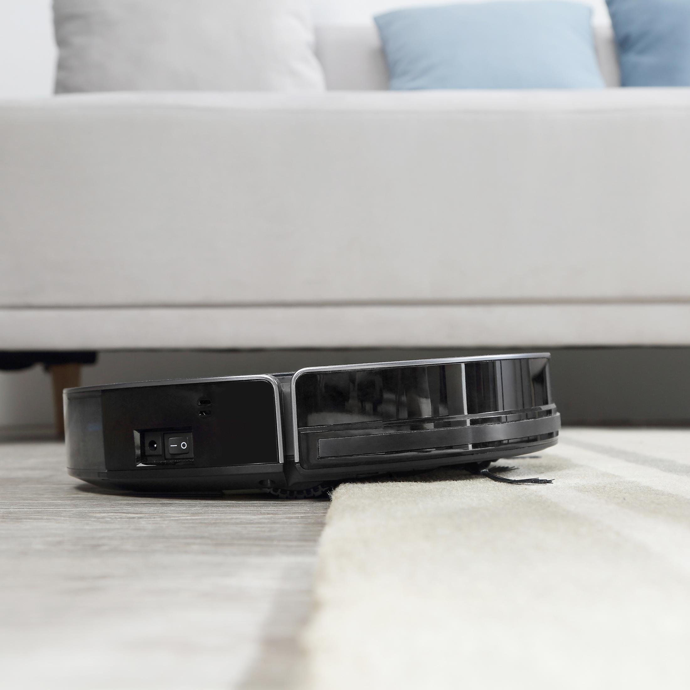 Schwarzer Roboter-Staubsauger, Seitenansicht, auf einem hellen Teppich. Ein weißes Sofa ist im Hintergrund.