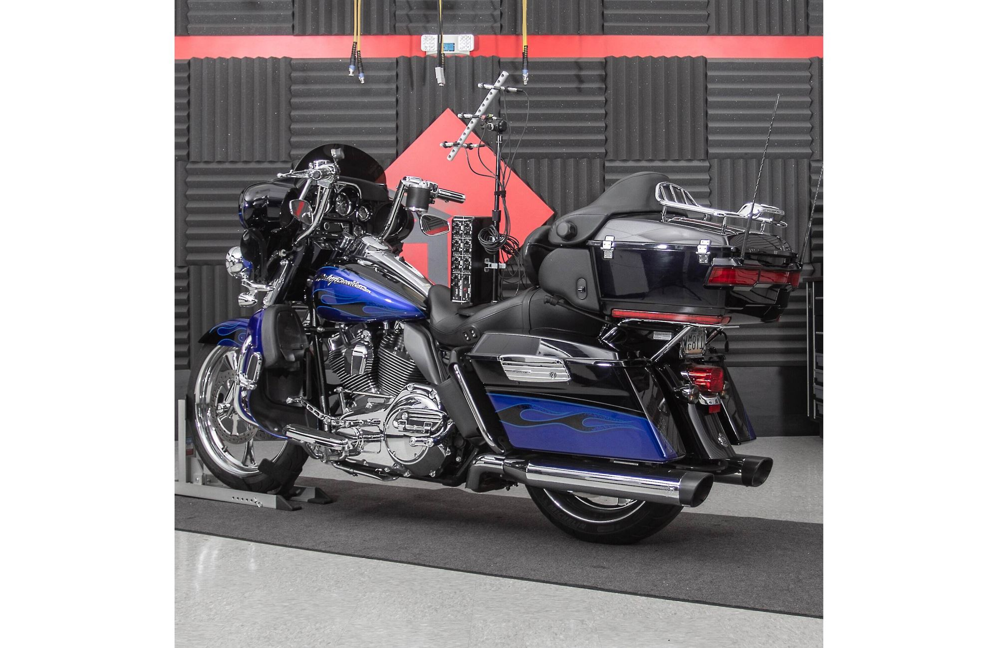 Blaues und schwarzes Harley-Davidson Motorrad. Es steht in einer Garage. Roter und schwarzer Hintergrund.