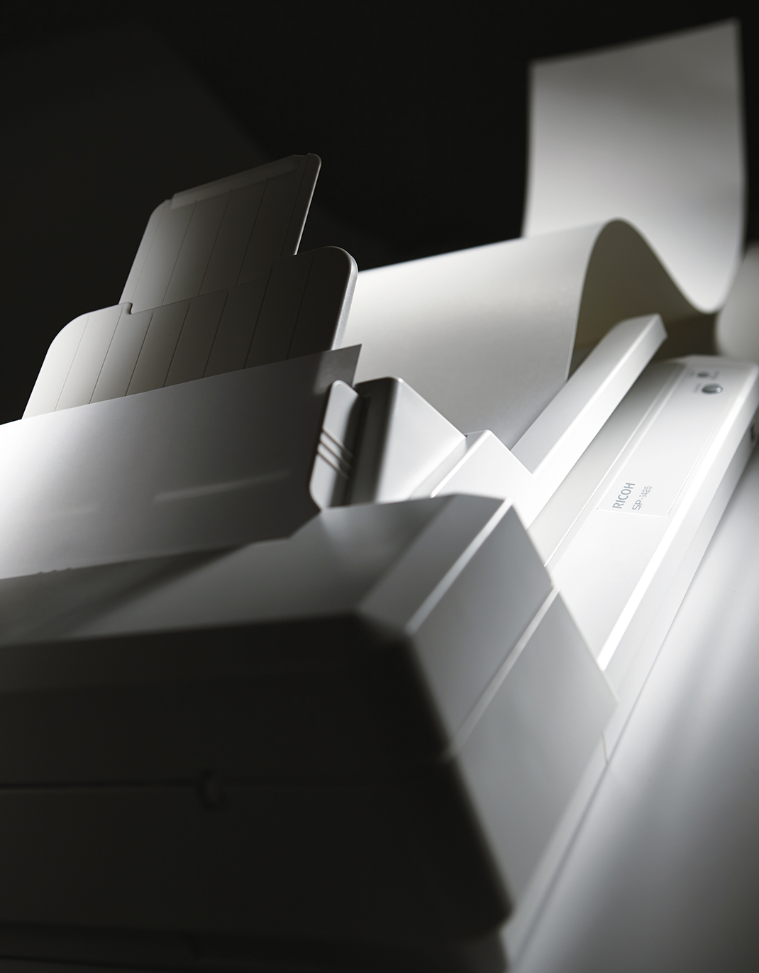 Zbliżenie białej drukarki z wychodzącym papierem. Oświetlenie tworzy cienie.