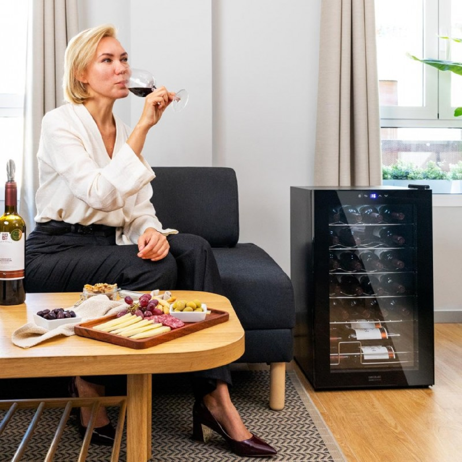 Donna che beve vino, seduta vicino a una cantinetta con snack.