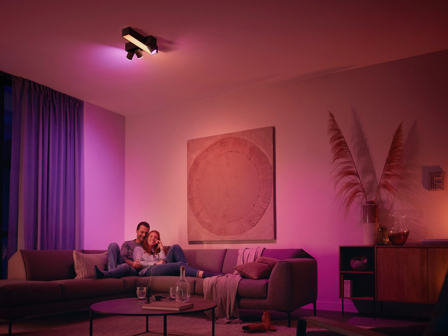 Een stel op een bank onder een lamp, met een schilderij aan de muur, de kamer is roze.