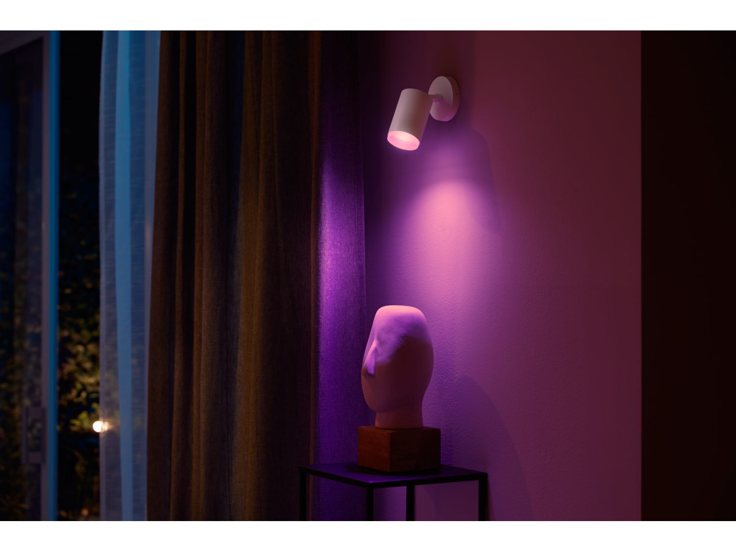 Witte spot op een muur, die een sculptuur verlicht. Paars lichteffect.