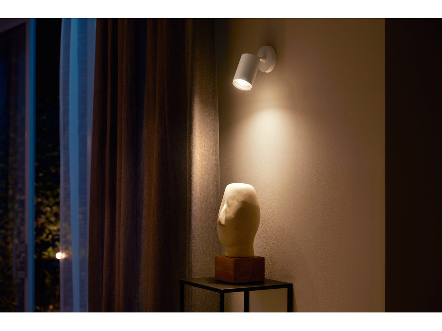 Witte wandspot die een sculptuur en tafel verlicht.