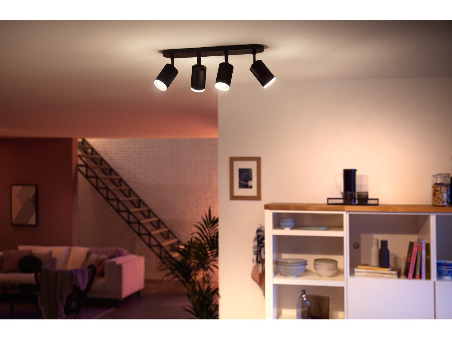 Plafond met spotlights. Een woonkamer met trap en witte meubels is zichtbaar.