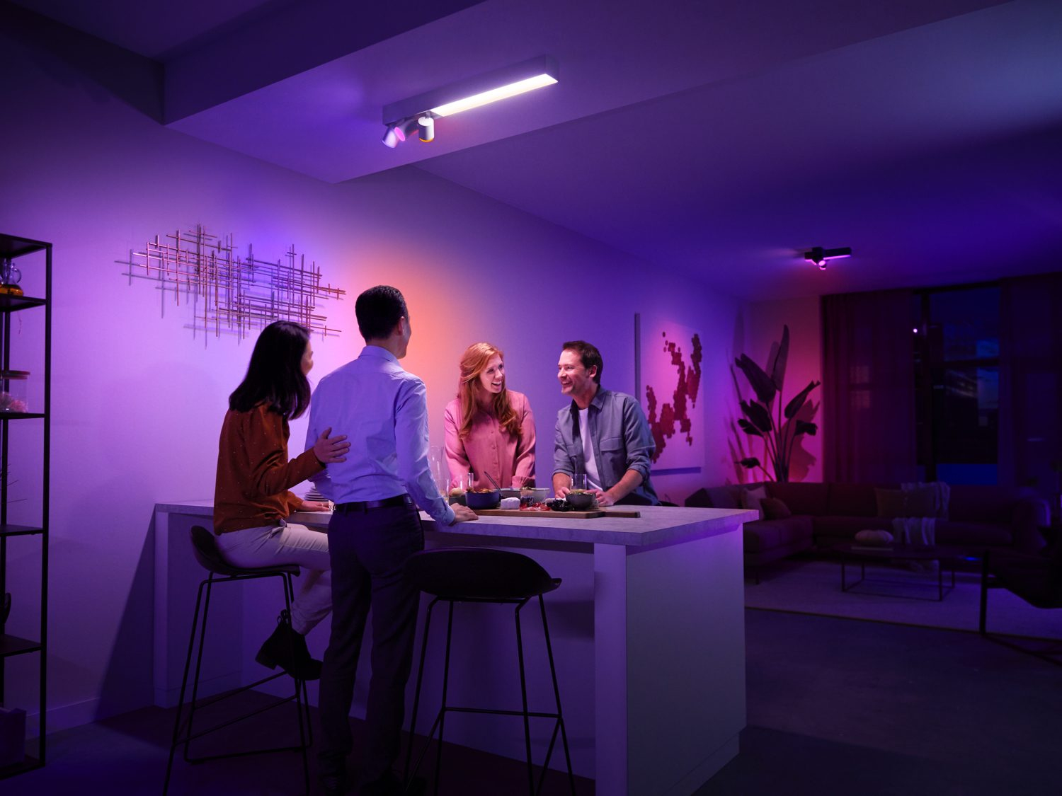Vier mensen in een kamer met kleurrijke verlichting. Ze staan bij een bar en praten.