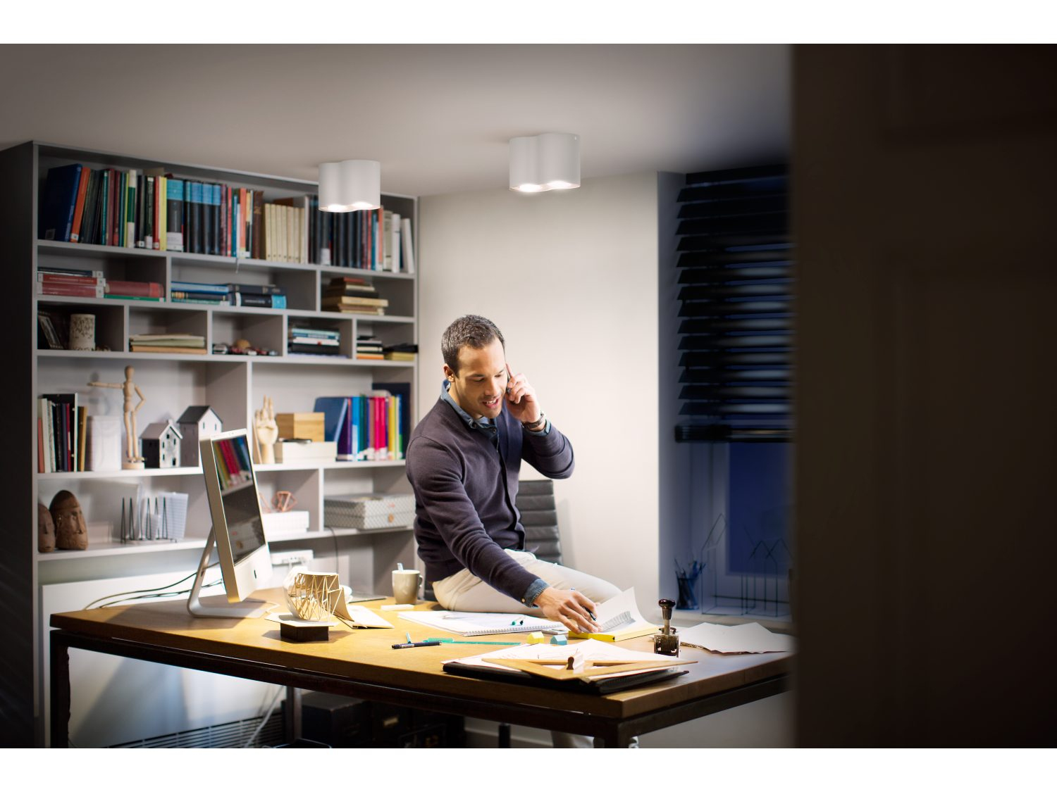 Mężczyzna na biurku w biurze z komputerem i książkami. Rozmawia przez telefon.