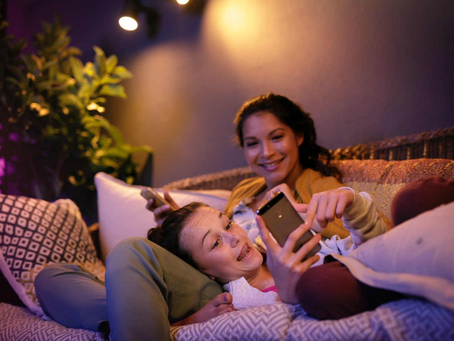 Dwie kobiety na kanapie patrzą na telefon. Jedna leży, druga siedzi.