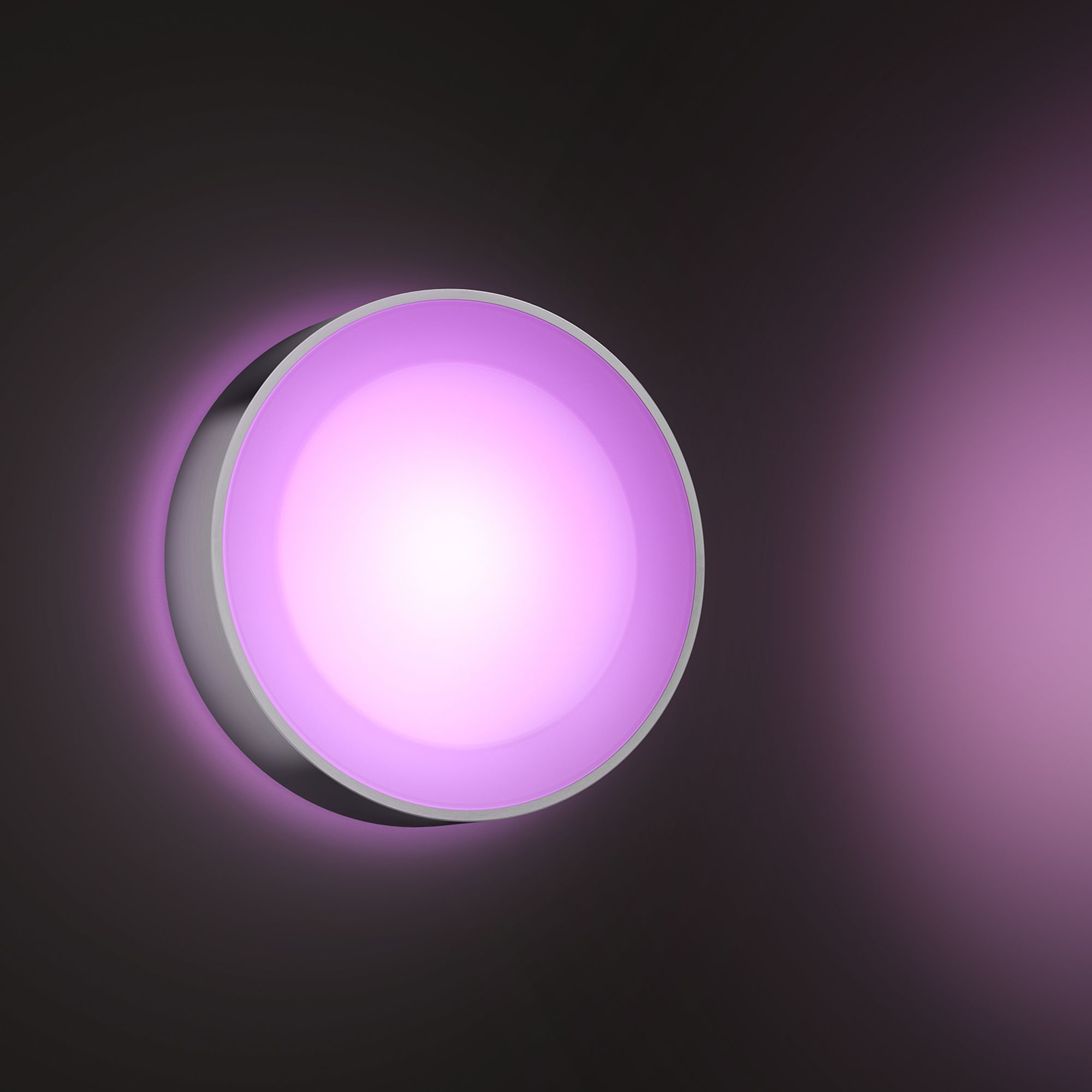 Ronde, zilveren wandlamp met een paarse gloed. Donkere achtergrond.