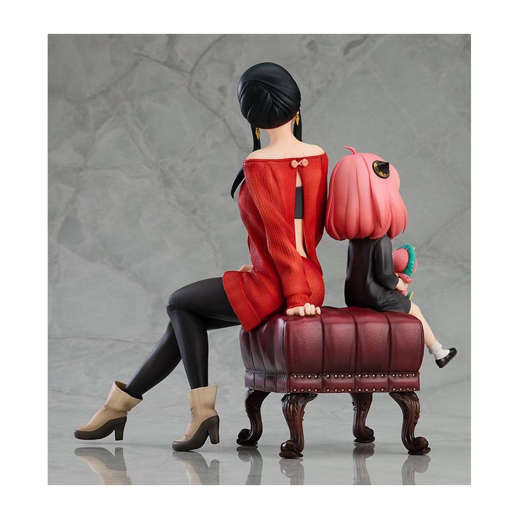 Figur einer Frau in rotem Kleid mit Kind. Sie sitzen auf einem weinroten Hocker.