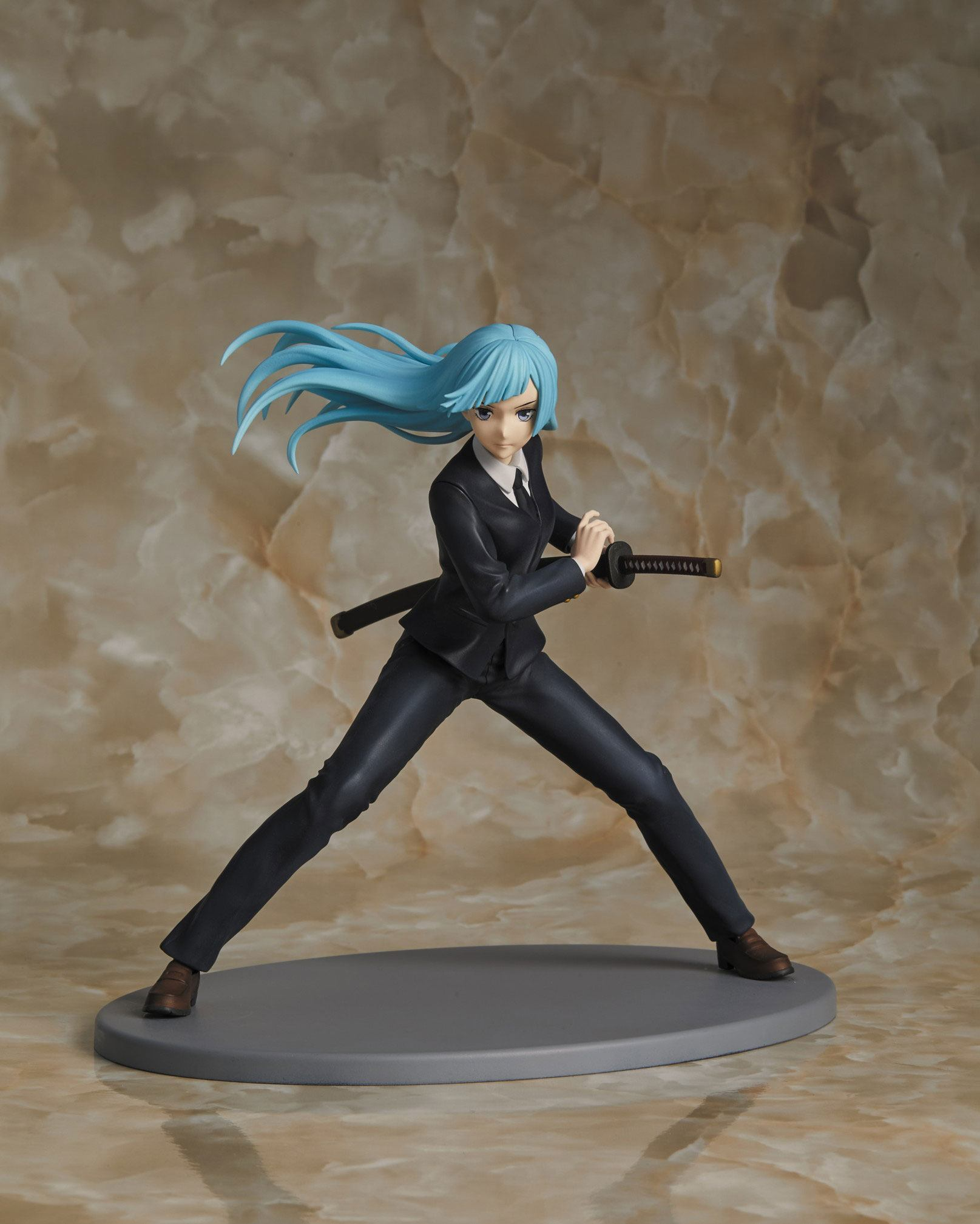 Figura de anime de una mujer con cabello azul en traje negro. Sostiene una espada y está sobre base gris.