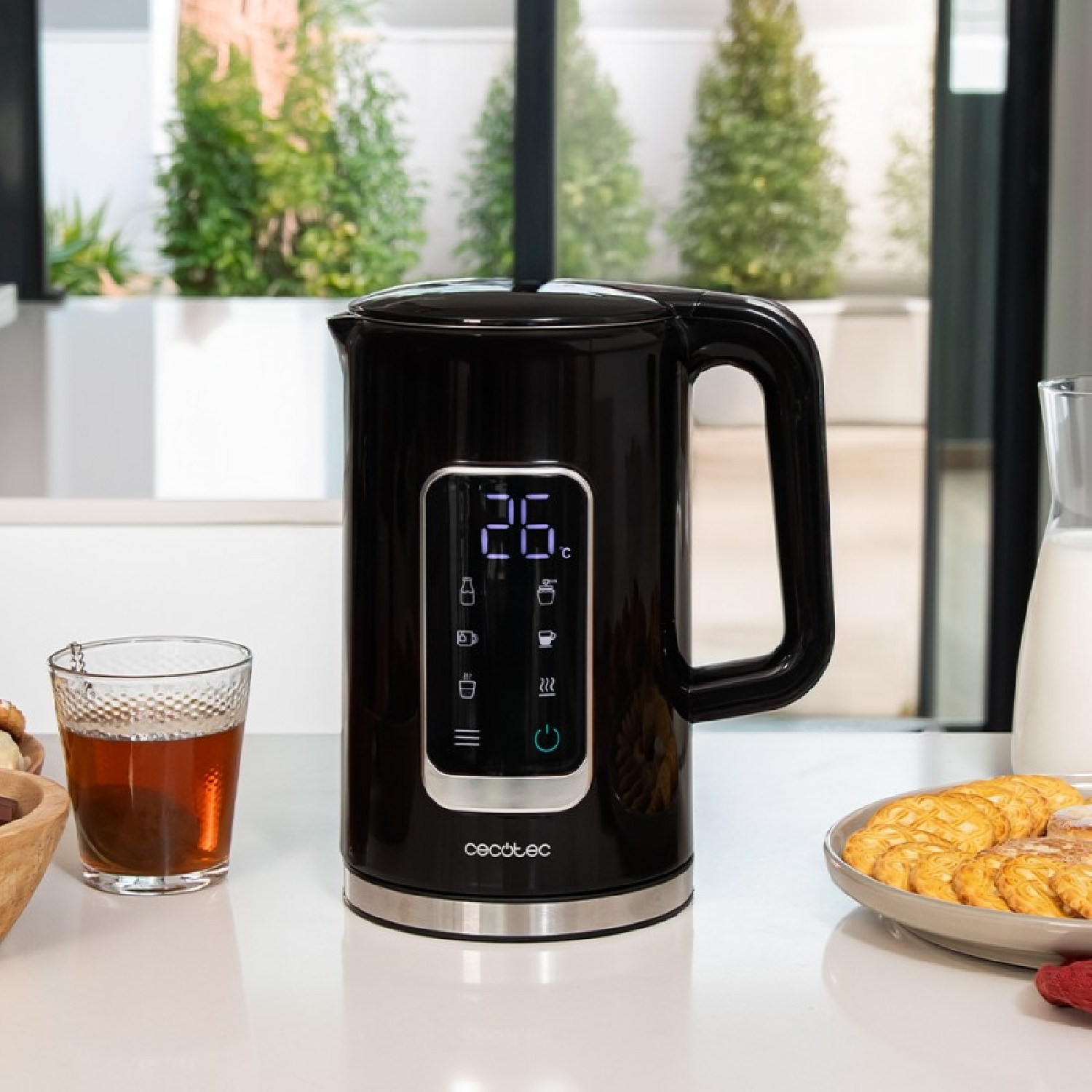Un bollitore elettrico nero con display digitale. È su una superficie bianca accanto a un bicchiere e un piatto.