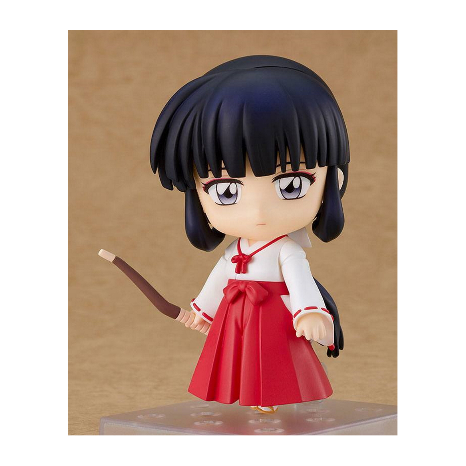 Eine kleine Anime-Figur eines Mädchens in rotem Rock und weißem Oberteil, das einen Bogen hält, vor beigem Hintergrund.