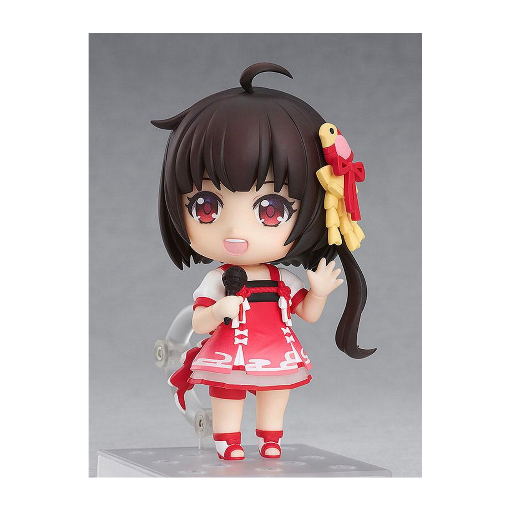 Chibi-Anime-Mädchenfigur mit dunklen Haaren, rotem Kleid und Mikrofon. Sie winkt, mit hellgrauem Hintergrund.