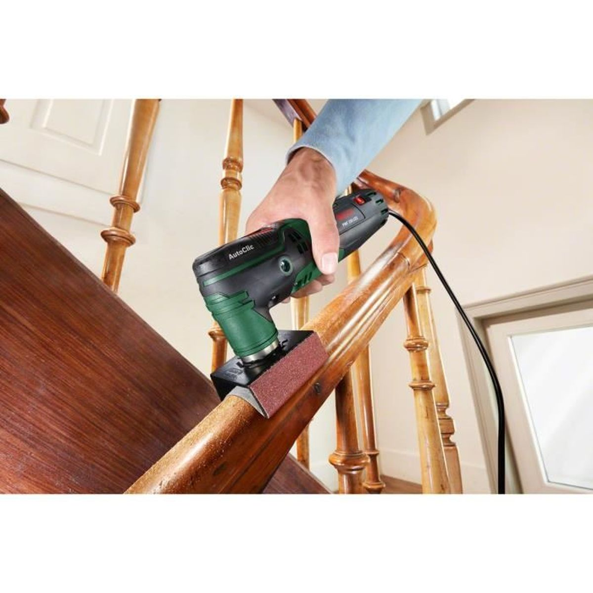 Eine Hand schleift einen Holzgeländer mit einem Elektrowerkzeug auf einer Treppe.