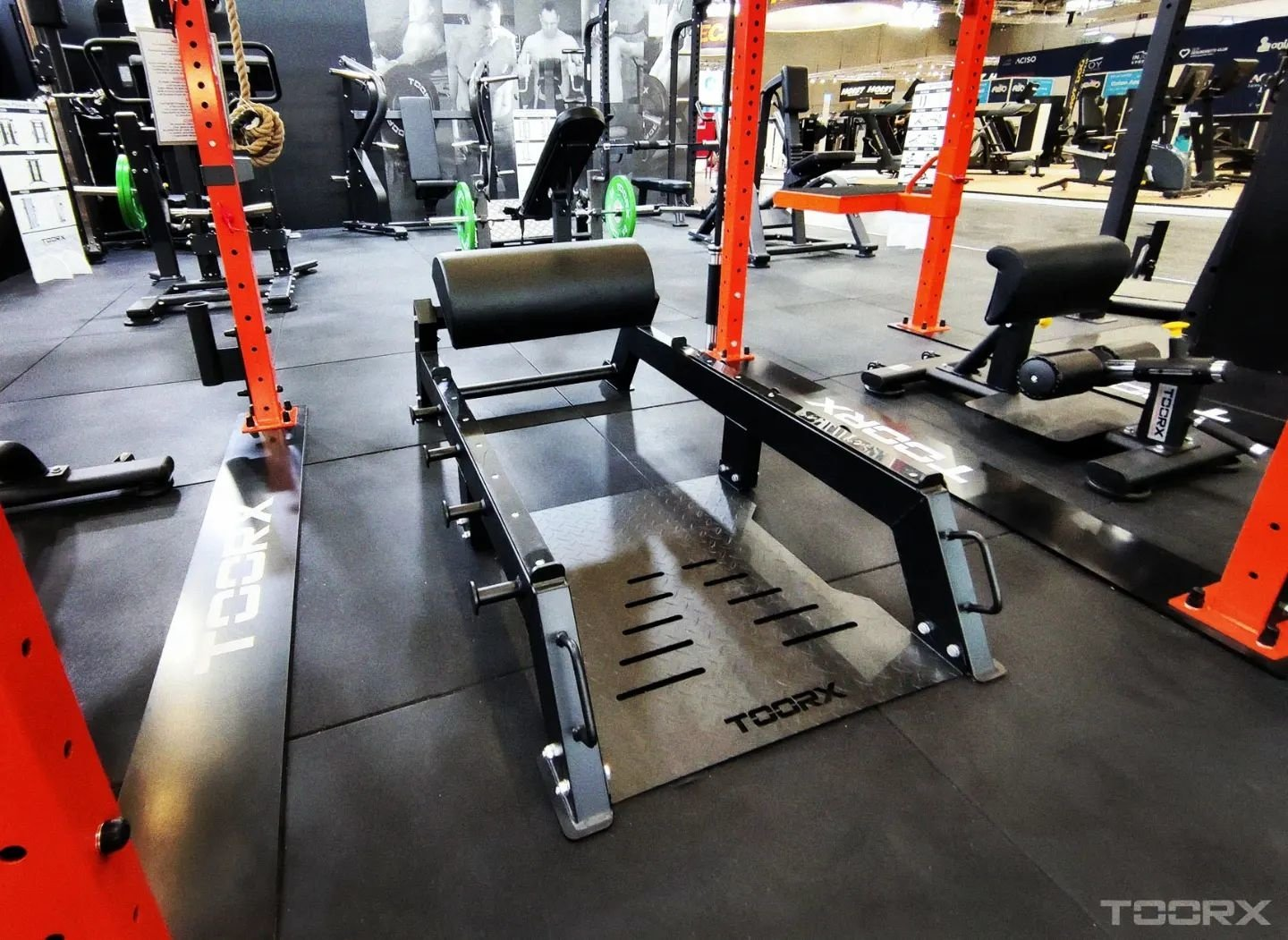 Gyminterieur met fitnessapparatuur. Een gewichtmachine staat centraal. Andere machines en gewichten op de achtergrond.