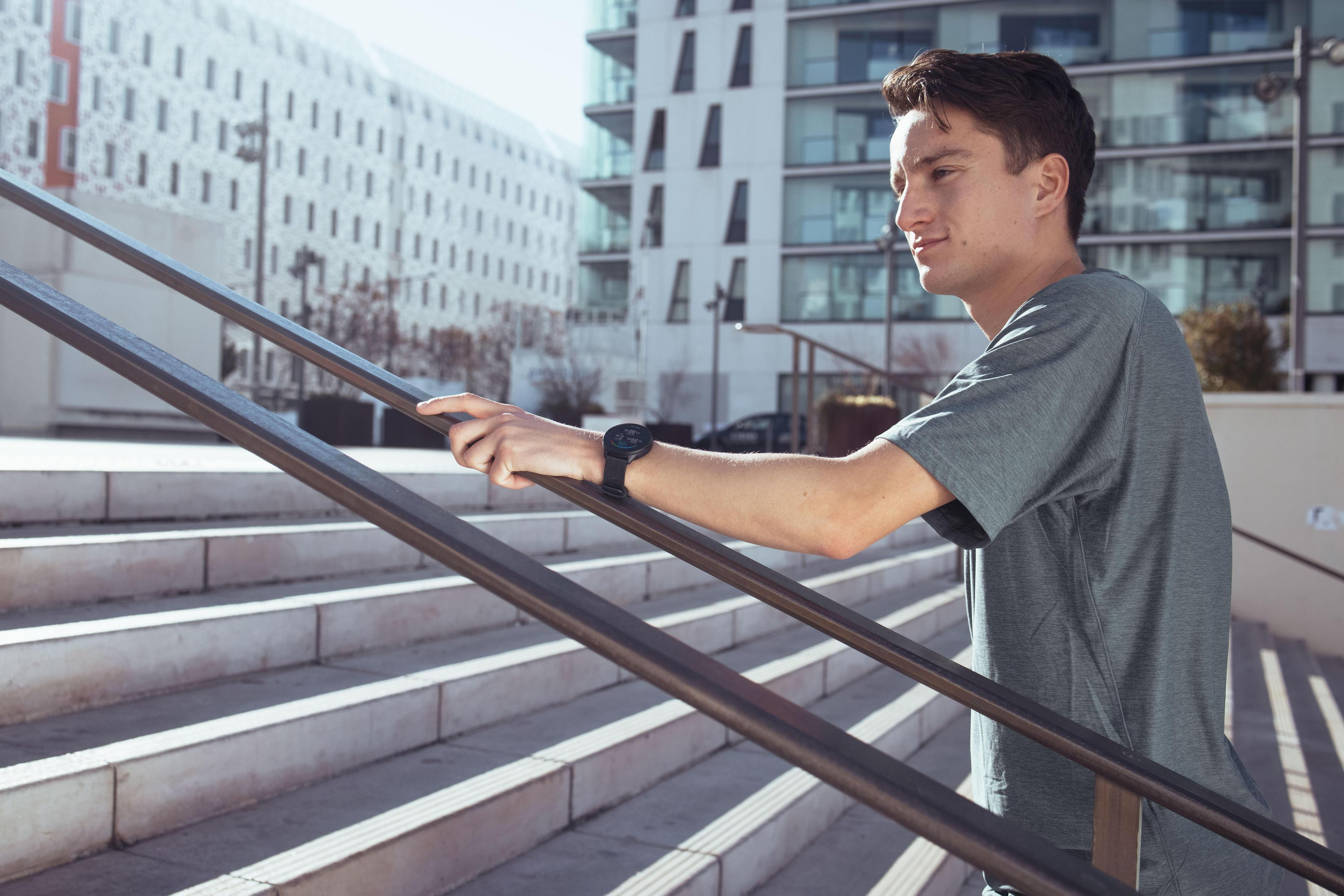 Mężczyzna w szarej koszuli wchodzi po schodach, nosząc czarny zegarek.