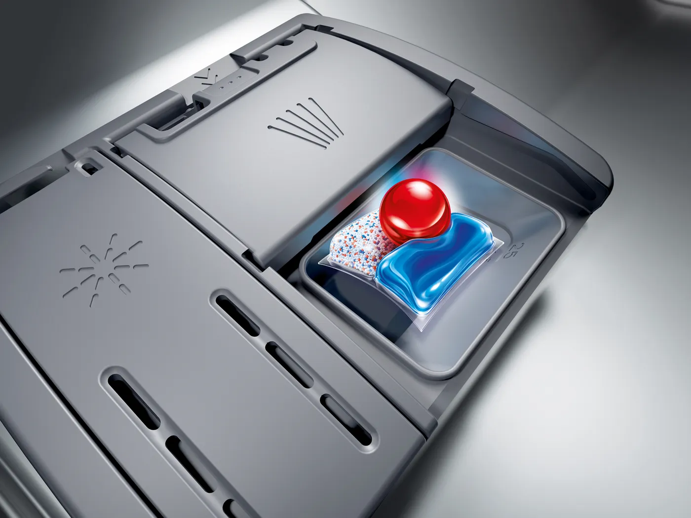 Geschirrspülfach mit einem Spülmittel-Pod, einer roten Kugel und einem blauen Reinigungs-Pod.