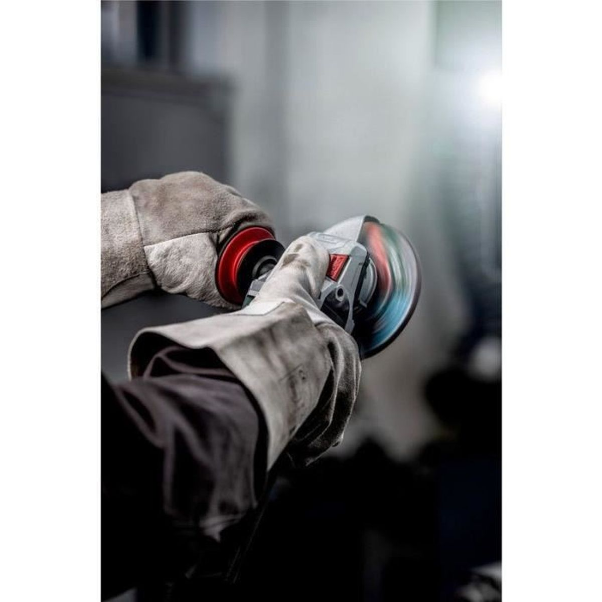 Osoba w rękawicach ochronnych używa szlifierki kątowej, lecą iskry, w warsztacie.