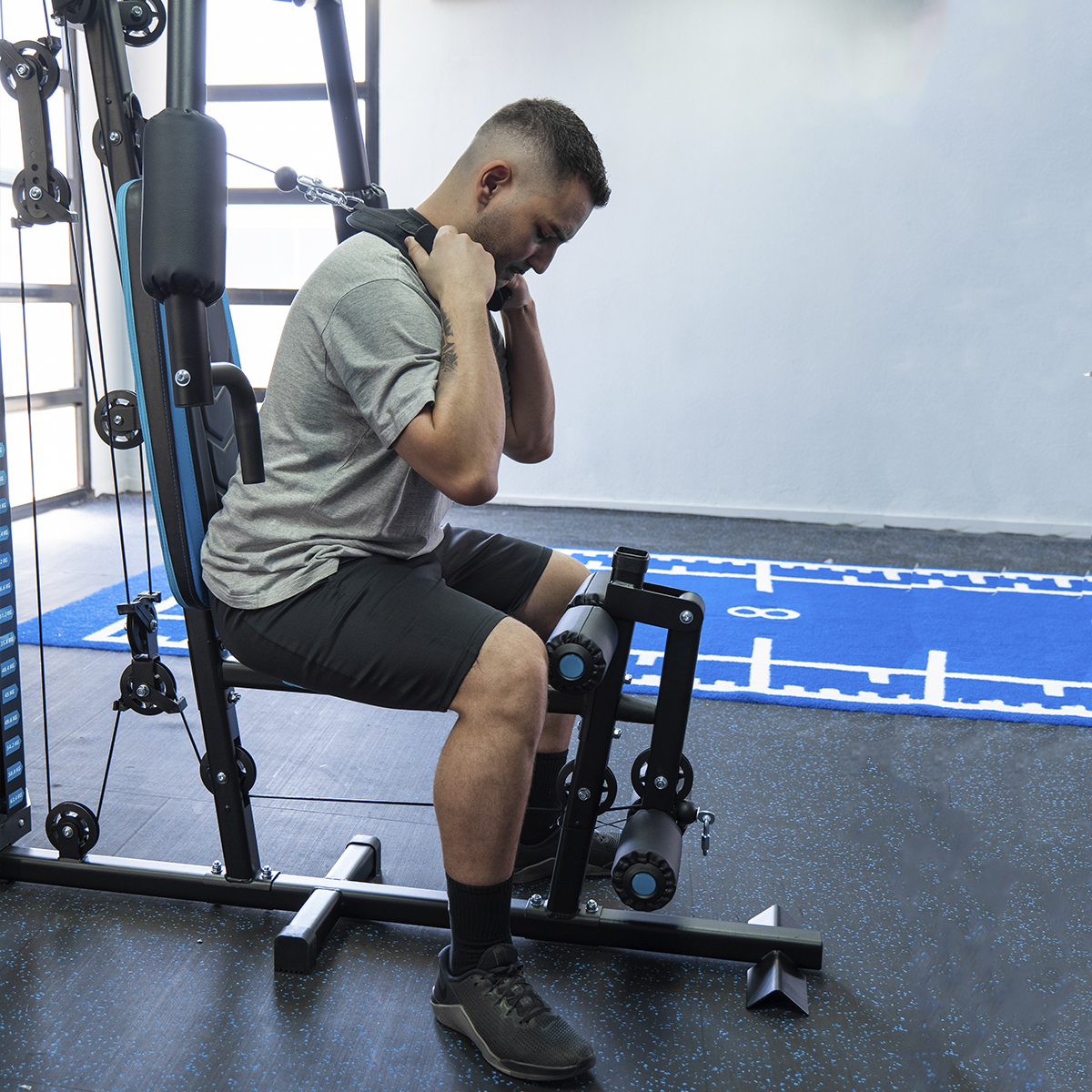 Un hombre haciendo ejercicio en una máquina de gimnasio. Está sentado y tirando de una barra.