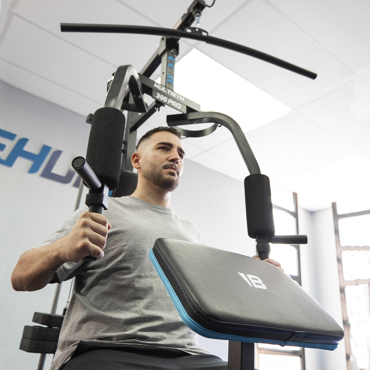 Un hombre usando una máquina multi-gimnasio, con una camiseta gris, mirando hacia arriba.